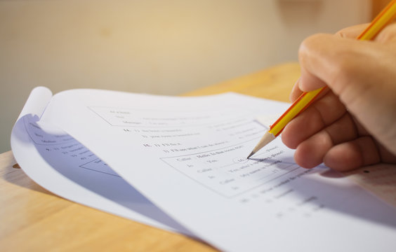 Students hands taking exams, writing examination room with holding pencil on optical form of standardized test with answers and english paper sheet on row desk chair doing final exam in classroom.