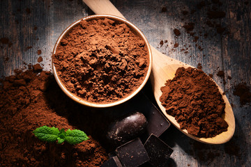 Composition with bowl of cocoa powder on wooden table