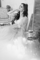 A girl in a beige peignoir, with a wreath of flowers on her head, poses in the studio loft, fine art wedding style