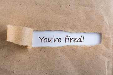 You are fired. Message in letter or note, appearing behind ripped brown paper of envelope text you are fired