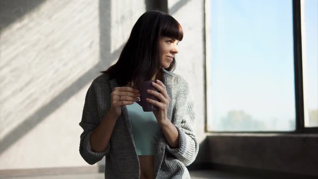 Attractive girl in a warm cardigan is enoying her day at home alone. She is drinking hot tea in autumn.