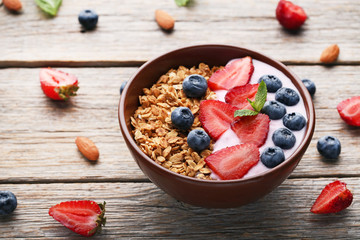 Tasty granola with berries in bowl on wooden table