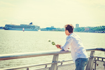 Man Welcomes You. Wearing white shirt, holding white rose, a guy standing by Hudson River in New York, opposite New Jersey, looking faraway. Boat, ship on background. Copy Space..