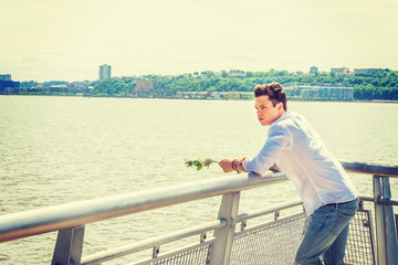Man Missing You. Wearing white shirt, jeans, holding white rose, a guy standing by Hudson River in New York, opposite New Jersey, looking at white rose on hands, thinking, lost in thought.  Copy Space