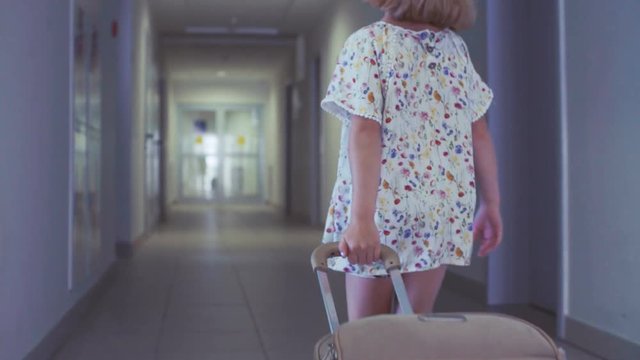 A little girl is rolling a suitcase in a hotel. Low angle shot.