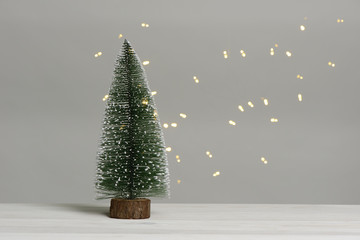 Árbol de navidad pequeño sobre mesa de madera blanca y luces desenfocadas