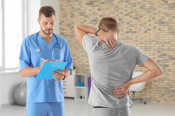 Fototapeta premium Physiotherapist with clipboard and young male patient in clinic