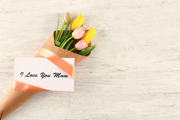 Bouquet of flowers with card for Mother's day on wooden background