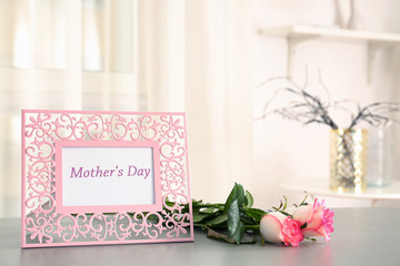 Frame with text MOTHER'S DAY and flowers on table