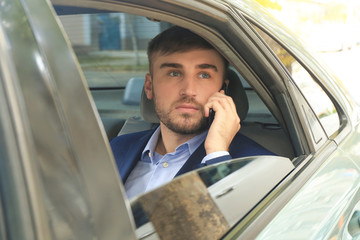 Young businessman talking by phone on back seat of taxi car