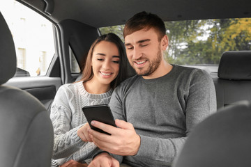Happy young couple with mobile phone on back seat of taxi car