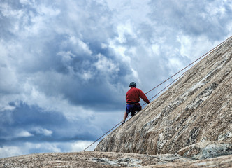 Mountain climbing instructor isolated against beautiful cloudy sky on rock incline
