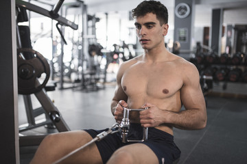 Rowing young man in gym training shirtless indoors