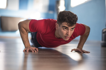 Young man trains push-ups in the gym on hands indoors