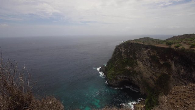 Cliff with waves crashing against rocky shore, Nusa Penida, Indonesia. Rocky coast and ocean with waves and rocky cliff. 4K video. Travel concept.