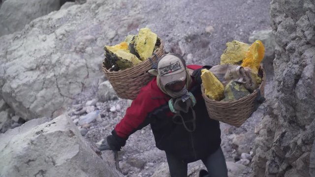 Worker carries a basket with pieces of sulfur on his shoulder. Sulfur miners carries sulfur from inside the crater of Kawah Ijen volcano in East Java, Indonesia.