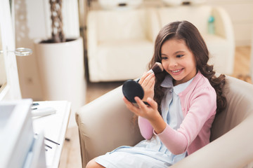 Beautiful little girl in beauty salon. The girl makes herself a make-up. She smiles and likes to look like her mother.