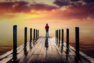 lonely man standing on a wooden pier during sunset facing mountain - 183103334