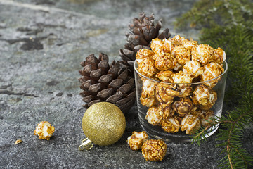 Appetizing golden caramel popcorn in paper striped cups in the New Year's interior with fir cones, New Year's golden balls on a gray stone modern background. Selective focus.