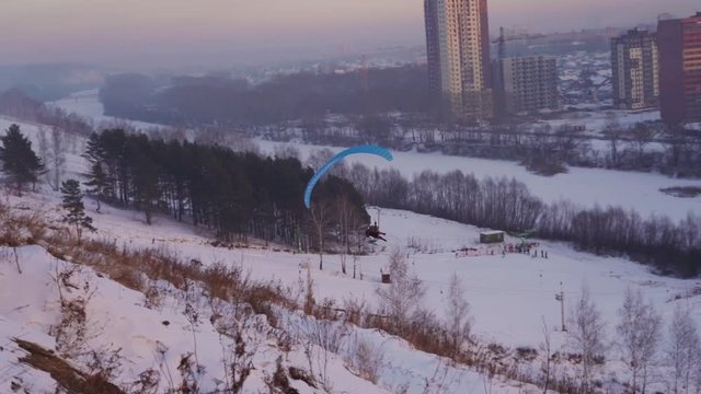 The paraplaner jumps with a running start and takes off over the snowy slope in the evening light