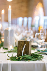 nature, catering, dining hall concept. small dark wooden cube with white number one on the front part of it, it is placed on the table for marking and surrounded with small conifer branches