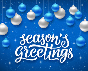 Seasons greetings script text on blue background with sparkles and colorful hanging balls. Vector illustration for holidays with lettering © aerial333