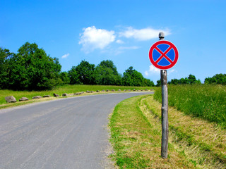 Prohibition sign of stop and parking on rural road. Metal road sign on a wooden pole. Countryside with field and trees.