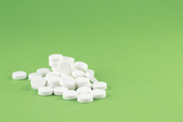 Close up white pills on pistachio green background with copy space. Focus on foreground, soft bokeh. Pharmacy drugstore concept