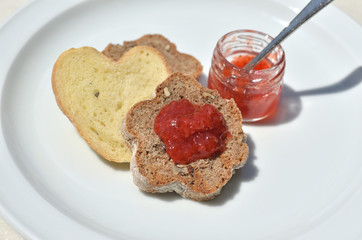 Pieces of domestic, home-made bread with whole grain and a small jar with delicious wild strawberry jam