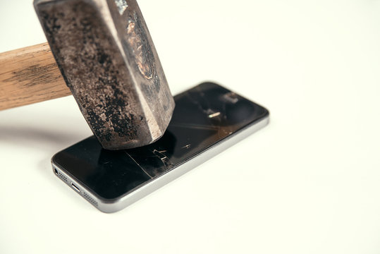 Big hammer breaks the screen of a modern smartphone. Broken glass screen of mobile phone. Crash of protect glass.