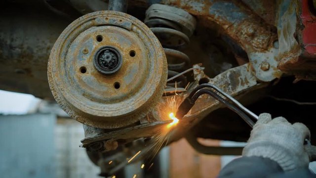 Close up shot of a worker uses a cutting torch to cut a large metal object into pieces at a metal recycling plant