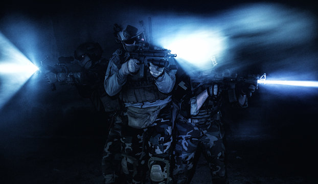 Squad of soldiers attacking in action under cover of darkness back light
