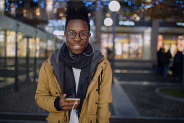 African man listen music in smartphone standing at dark night city, he smiling to camera