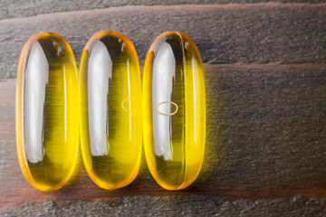 Yellow capsules omega 3, fatty acid, fish oil on dark wooden table, macro image, top view