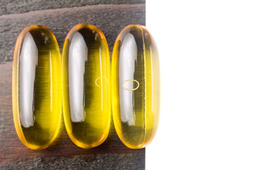 Yellow capsules omega 3, fatty acid, fish oil on dark wooden table with white card for your text, macro image, top view
