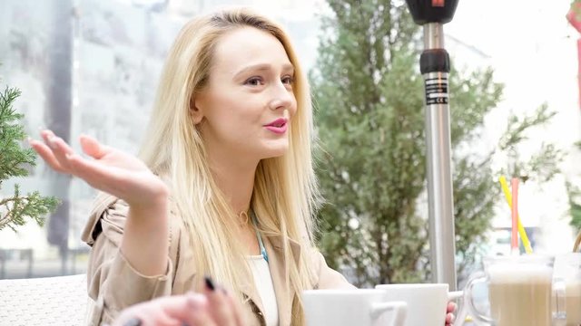 Beautiful blonde woman at cafe terace talking with her friends. Friendship and restaurant