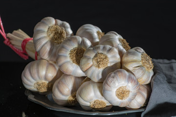 String of french pink garlic on old tin plate on black background