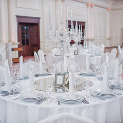 The crystal and glass candelabrum stands in the middle of the festive table at the banquet. The candles burn on it.
