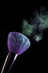 Photo of brush for makeup with purple pile and green make-up shadows in motion in studio on a black background