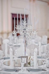 The crystal and glass candelabrum stands in the middle of the festive table at the banquet. The candles burn on it.