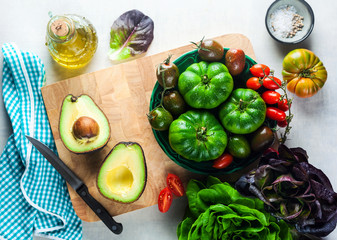 ingredients for salad from different types of tomato, avocado and arugula on a white stone table. cutting board, olive oil and condiments. healthy food, summer or spring menu