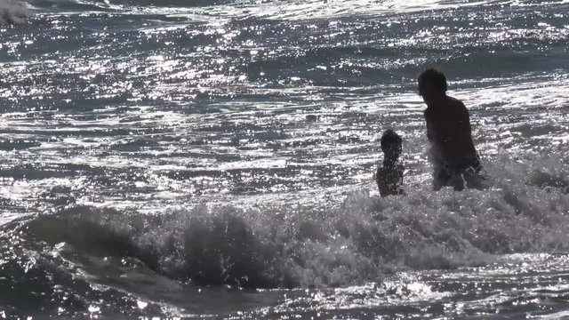 Father and son bathe among the waves of the silvery ocean