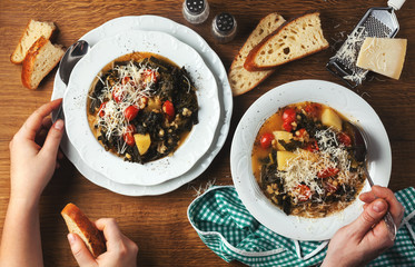 Curly kale (or cavolo nero) and barley soup. Winter Vegetable Soup on a wooden table and fresh homemade bread. men's and women's hands that eat