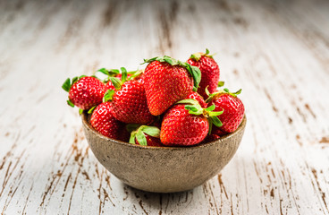 Bowl with fresh colorful organic strawberries fruit against wooden background. Healthy food, vegan and vegetarian concept.