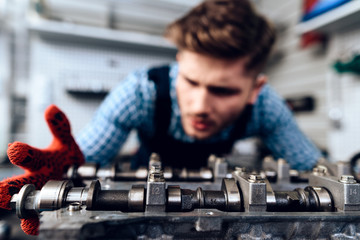 A young man works at a service station. The mechanic is engaged in repairing the car.