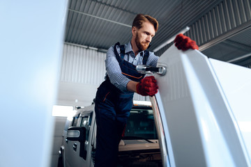 Red-haired man works at the auto service. The mechanic is engaged in repairing the car.