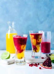 two glasses of alcoholic cocktail with orange liqueur, freshly squeezed pineapple and pomegranate juice and lime and ice on the table.