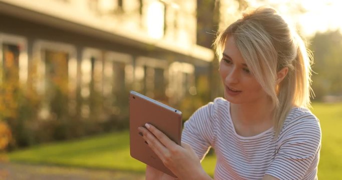 Young female student using tablet computer in the park. Girl doing online shopping on tablet pc