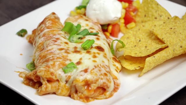 Adding a scoop of sour cream to a plate of chicken enchilada with tortilla chips.