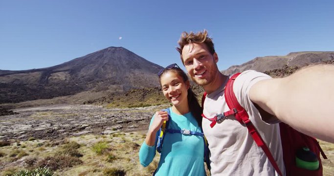 Happy Backpacking Couple Taking Selfie Video on Travel on New Zealand Hiking Tongariro Alpine Crossing. Couple photographing themselves by volcano. Beautiful landscape in Tongariro National Park.